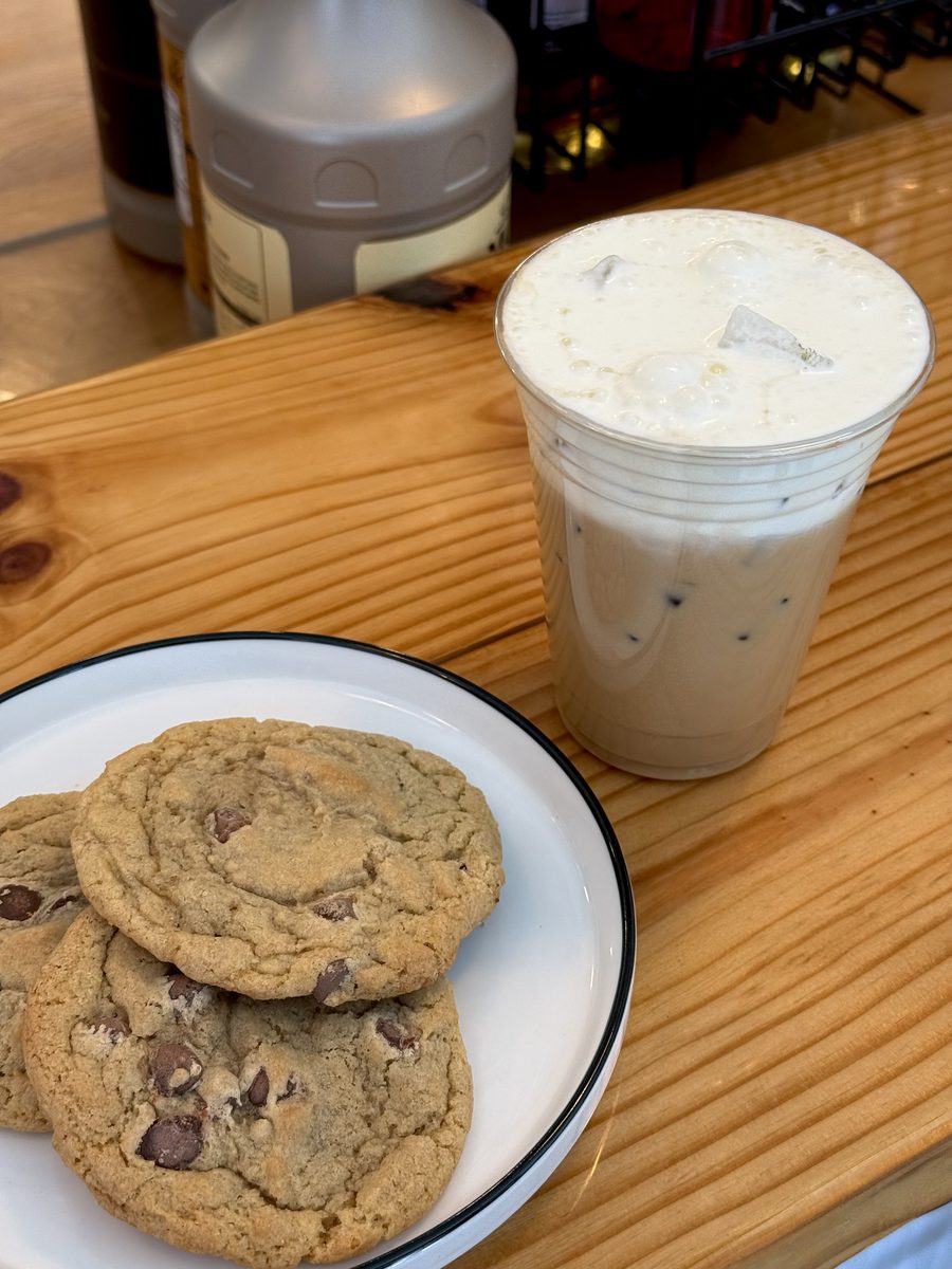 An iced latte beside two chocolate chip cookies on a plate on the counter