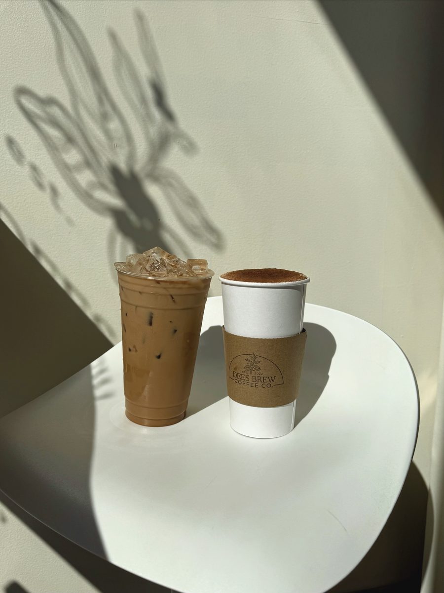An iced coffee and a hot cup on a white table with leaf shadows across it