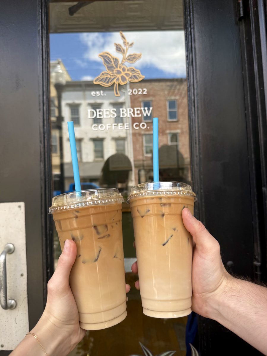 Two hands holding iced coffees in the doorway, under the Dees Brew window lettering